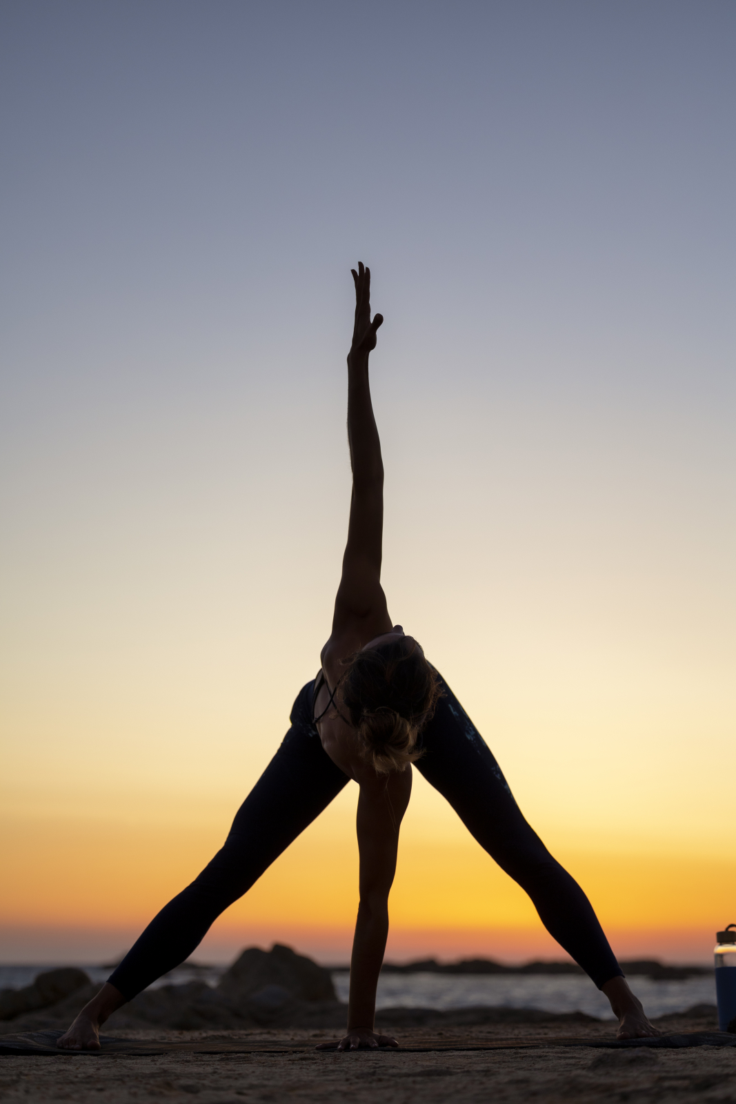 Ines Lamour doing Revolved Wide Legged Forward Bend Pose in front of a sea sunset